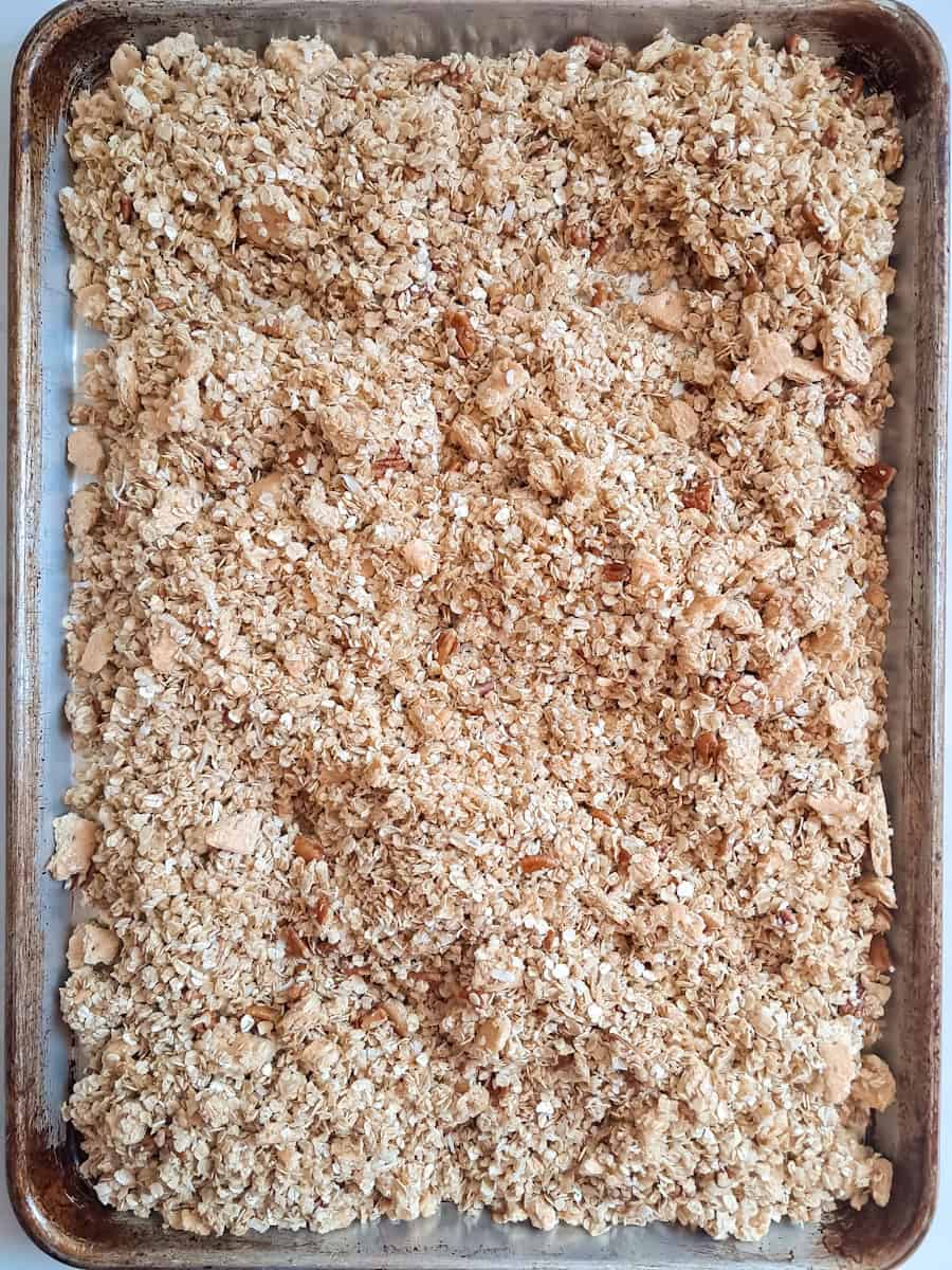 homemade granola is spread on a large baking sheet ready to toast.