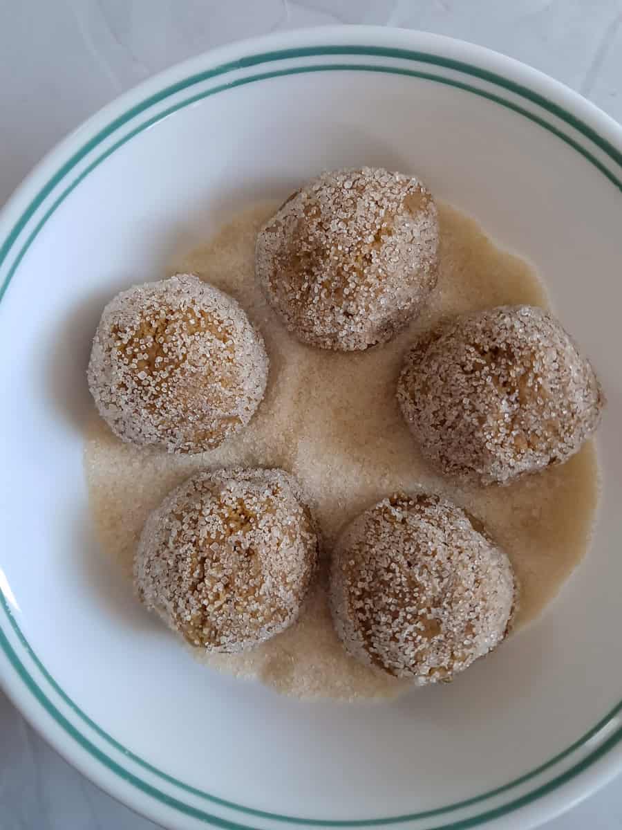 balls of cookie dough in a bowl of sugar.