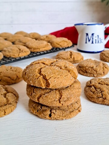 a stack of Amish molasses cookies with more chewy molasses cookies scattered around and a jar of milk.