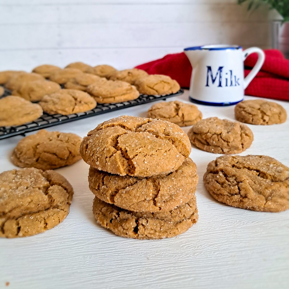 a stack of Amish molasses cookies with more chewy molasses cookies scattered around and a jar of milk.