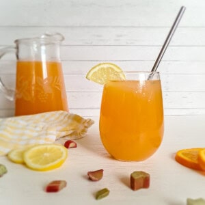 a glass cup and a pitcher of Amish rhubarb punch with rhubarb, lemon, and orange juice.