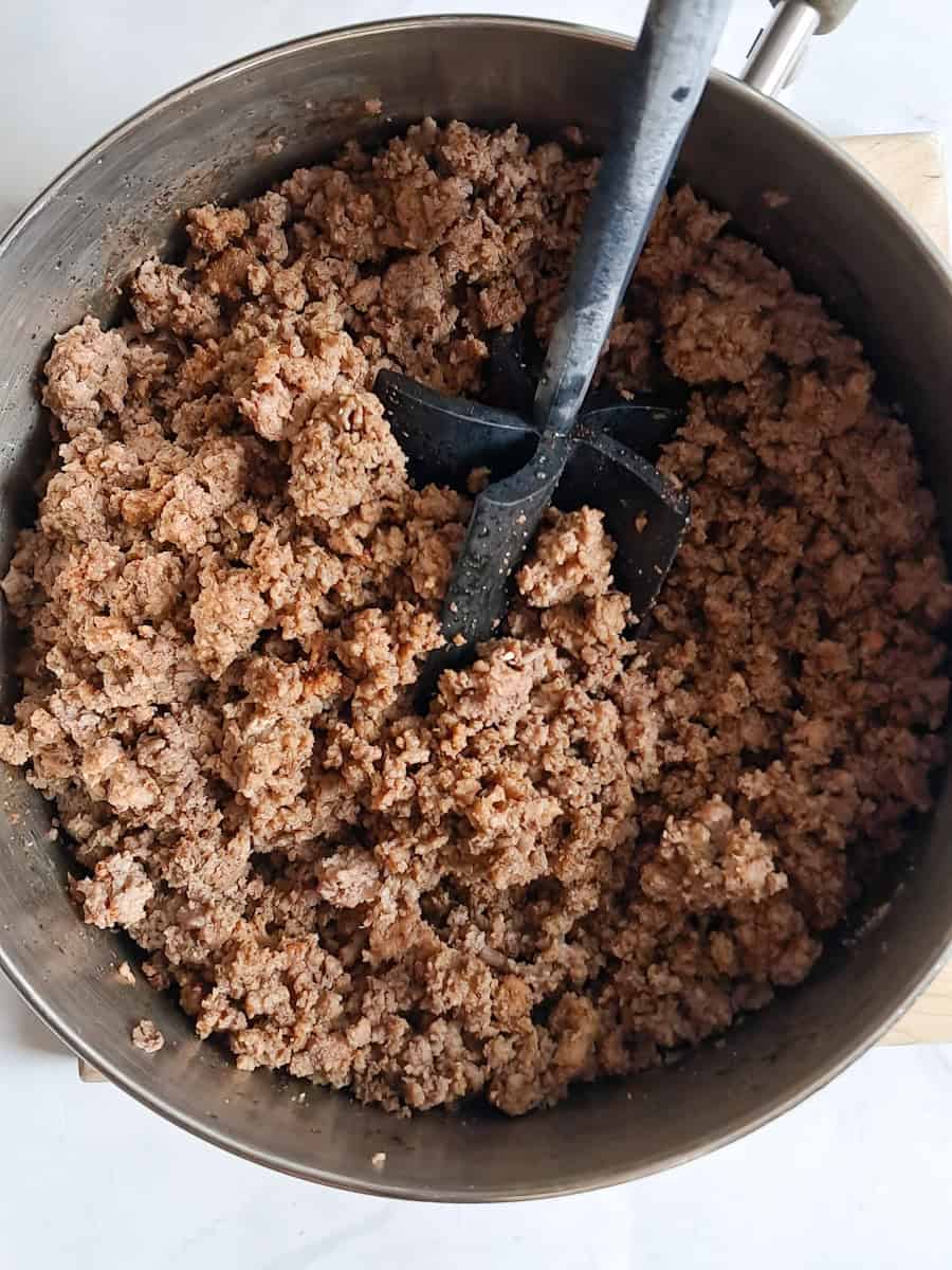 browned ground beef in a large saucepan with a meat chopper.
