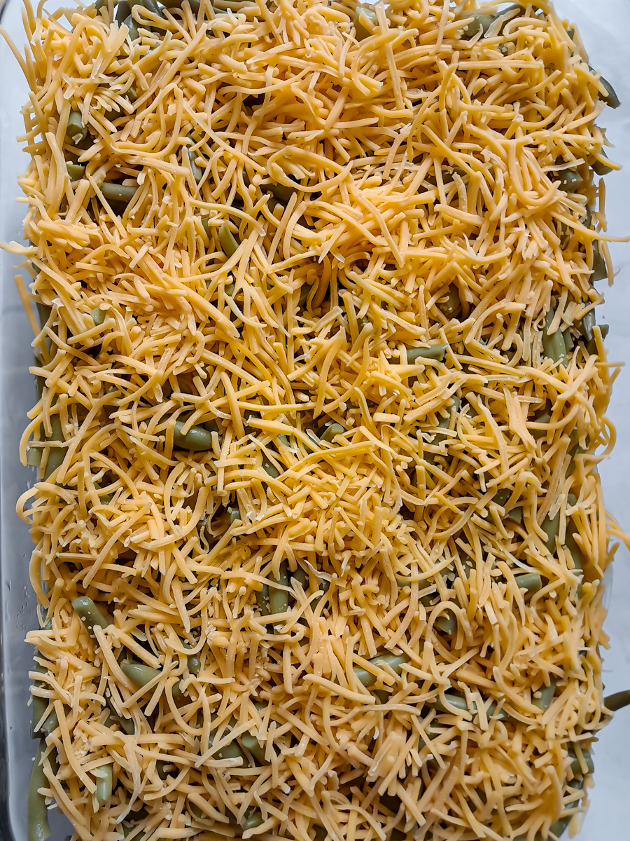 shredded cheese is spread over the top of the beef, cream soups, and green beans.