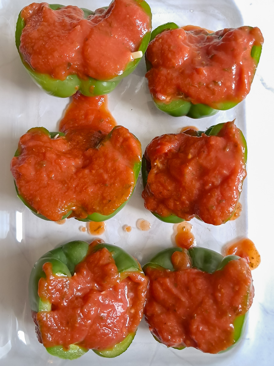 green bell peppers stuffed with ground beef and rice mixture and covered in sauce, ready to bake.