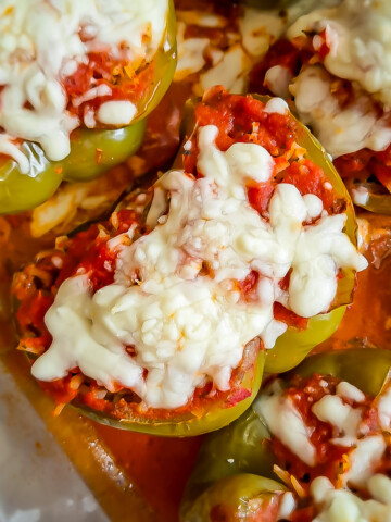 stuffed green peppers with ground beef and rice and topped with sauce and cheese in a 9x13" pan