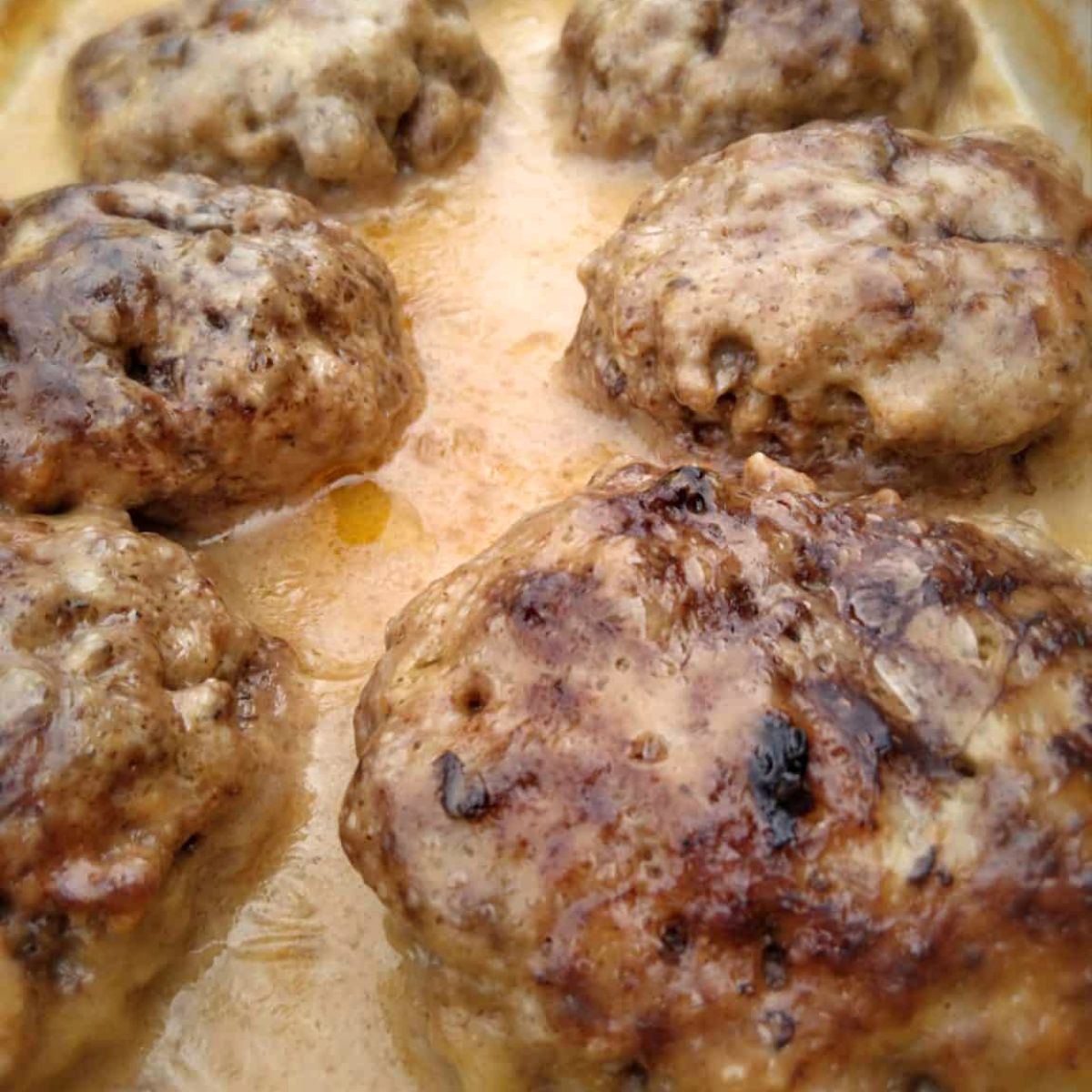 a close-up look at a pan of poor mans steak patties in mushroom gravy - an easy and affordable ground beef favorite.