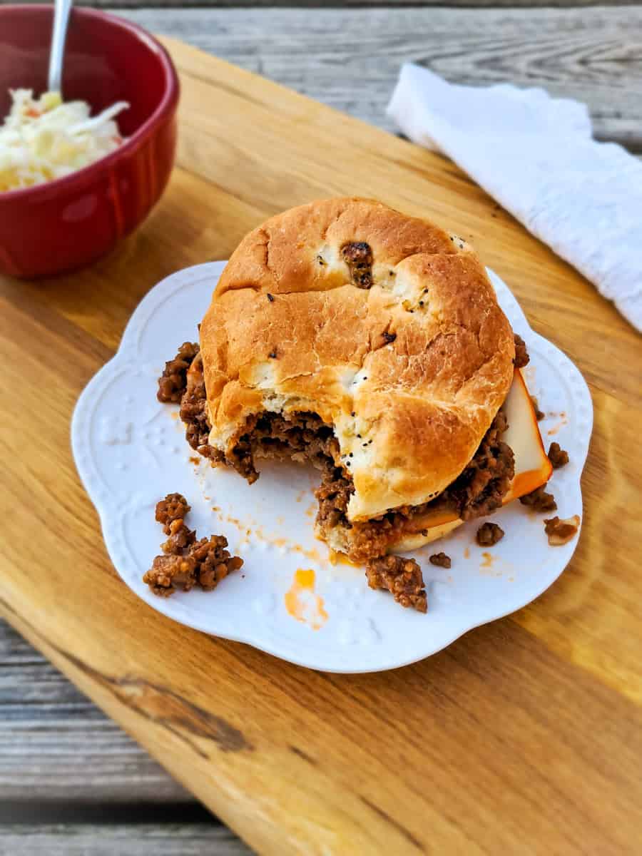 a sloppy joe sandwich with a bite taken out, and a bowl of coleslaw on a board.