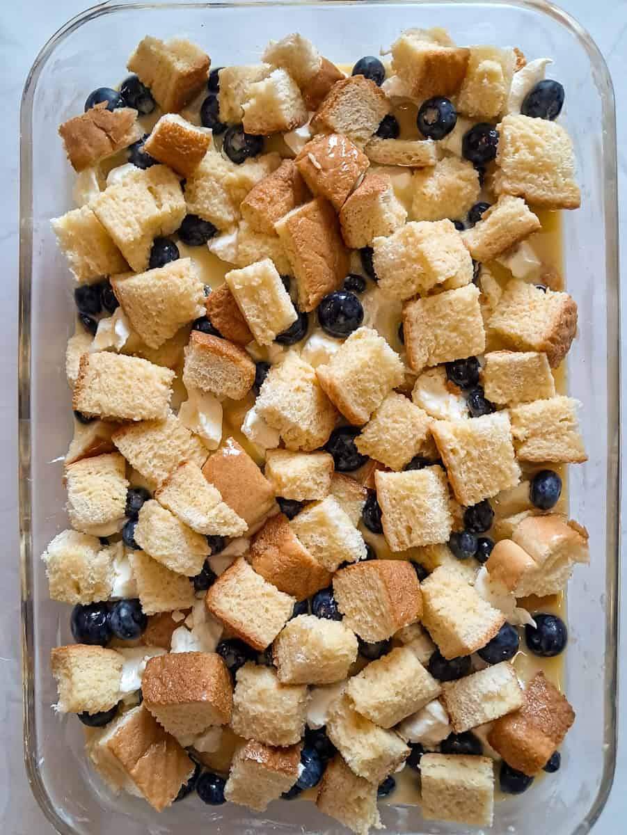 stuffed french toast with bread cubes, blueberries, cream cheese, and the egg mixture is assembled in a baking dish, ready to refrigerate overnight.