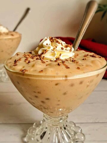 small bowls of homemade butterscotch tapioca pudding in goblet dishes with whipped cream and chocolate shavings on top.