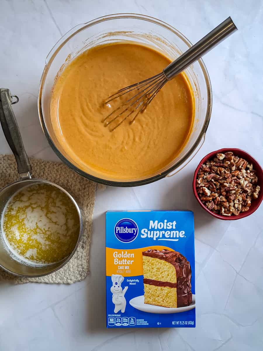 a large bowl of pumpkin mixture for the bottom layer, melted butter in a saucepan, chopped pecans in a small dish, and a boxed cake mix.