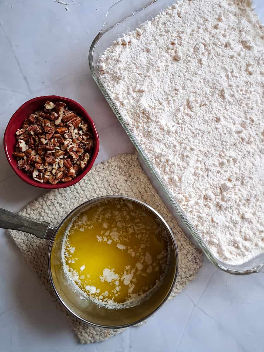 pumpkin mixture in the bottom of a 9x13" pan with dry cake mix spread on top, butter in saucepan, and chopped pecans in a small bowl.