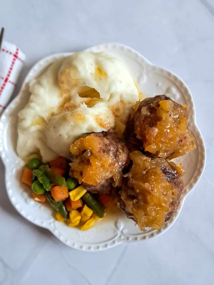 a plate with ham balls, mashed potatoes, and mixed veggies.