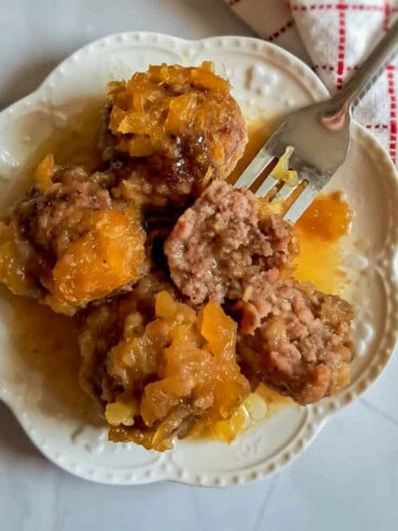 a plate full of pineapple glazed PA Dutch ham balls, one is cut open so that you can see the inside of the balls.