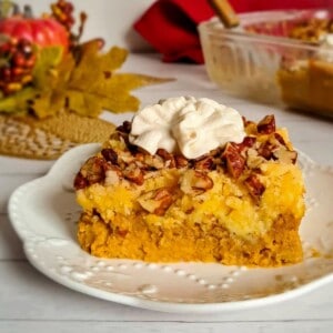 a small plate with a serving of pumpkin pie upside down cake topped with pecans and whipped cream.