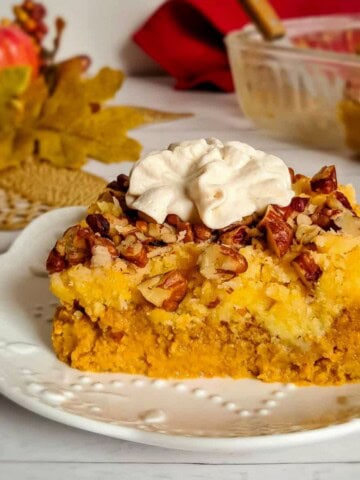 a small plate with a serving of pumpkin pie upside down cake topped with pecans and whipped cream.